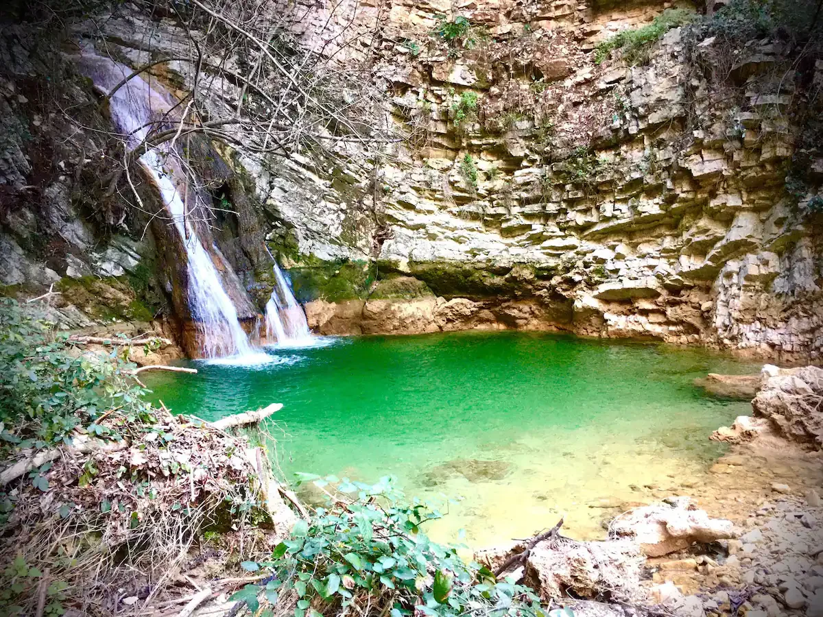 La cascata del Santuario della Ninfa che scende tra le rocce nella pozza verde